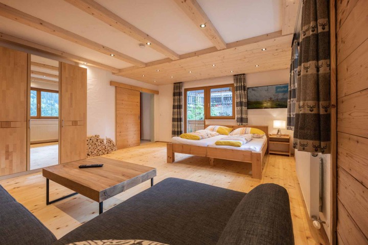 Vacation apartment with warm wooden walls and a comfortable bed in the room as well as a couch and access to the bathroom