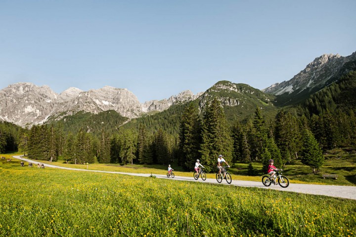 Family members cycle along a mountain path in the Stubai Valley, surrounded by impressive mountain scenery.
